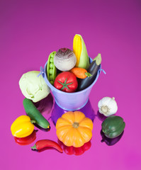 Fake small vegetables in bucket on neon background.