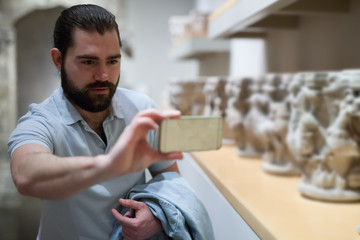 Bearded man photographs museum exhibits using smartphone