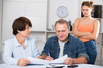 Obraz premium Smiling parents are reading utility bill with their adult daughter