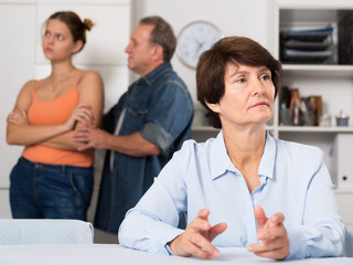 Man and his daughter are sympathying their sad mother who is sitting at the table