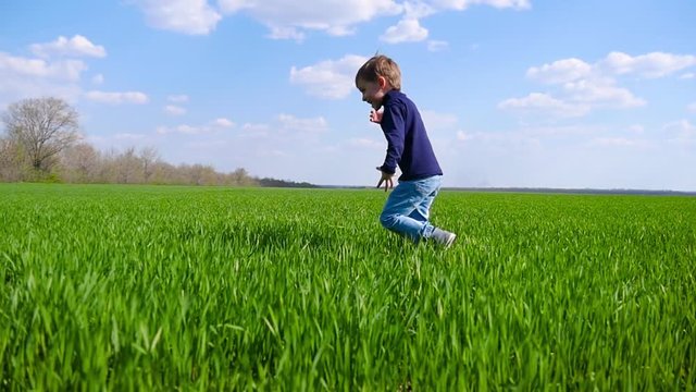A happy child runs across a field of green grass and kicks a soccer ball in slow motion