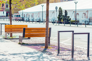 Two wooden empty benches on the sidewalk downtown during a bright day with trees and car in background – Resting place in the city near the street