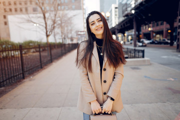 Fototapeta premium Beautiful girl in a city. Stylish brunette in a brown coat. Woman in a Chicago