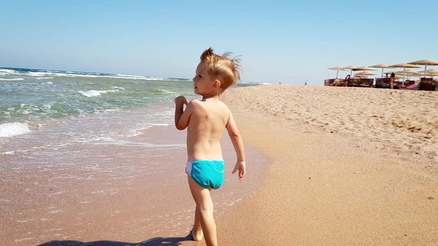 4k video of little toddler boy walking on the sand beach at sea