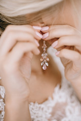 Elegant blonde bride putting on earrings closeup, preparing for wedding