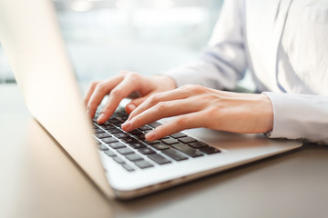 Young businesswoman using computer in office. Female hands typing on laptop keyboard. Blurred background