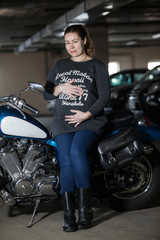 Motorcyclist pregnant woman sitting on chopper bike and holding her belly, parking lot