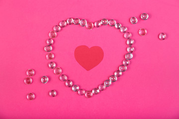 A heart lined with beads on a pink background with a heart in the middle in a frame of beads.