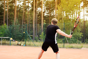 Male tennis player in action on the court in the evening sunset
