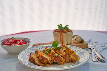 Baked egg pie or kind of quiche, french style dish served on rustic plate with fresh tomato salad. Made from eggs, smoked ham, parsley, pork meat and bread. Traditional spring food in Czech Republic.