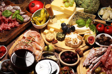 Italian antipasti wine snacks set. Cheese variety, Mediterranean olives, crudo, Prosciutto di Parma, salami and wine in glasses over grunge background.