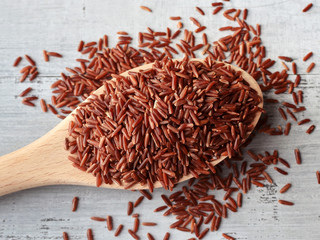 red rice on wooden spoon over wooden background