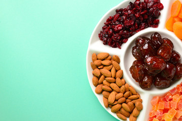 Mix of dried fruits and nuts on a white plate. Apricot, almond, raisin, dates fruit. On a green background. Space for text or design.