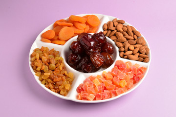 Mix of dried fruits and nuts on a white plate. Apricot, almond, raisin, dates fruit. On a lilac background. Space for text or design.