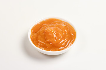 Orange sauce in white plate on white background.