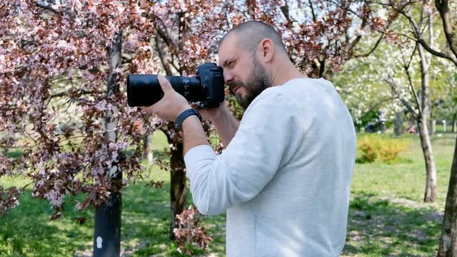Portrait of happy bearded photographer with blooming sakuras on a background
