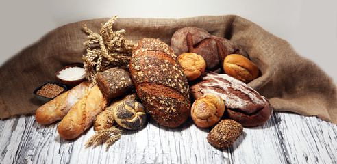 Assortment of baked bread and bread rolls on rustic white bakery table background