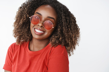 Waist-up shot of bright and happy african-american girl enjoying sun spending day outdoors wearing stylish new sunglasses and smiling broadly as looking happily at camera over white background © Cookie Studio