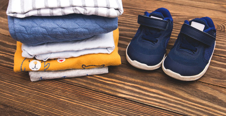 Folded bodysuits with sneakers on wooden background. Stack of children's clothes.