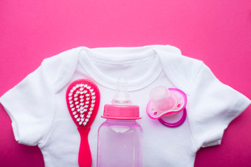 Newborn baby story. T-shirt and children's toys, scissors, baby bottle, nipple, hairbrush on red background