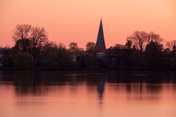 Fototapeta na wymiar Red and orange Sunrise over city of Eutin with silhouette of churchtower and trees, Schleswig-Holstein