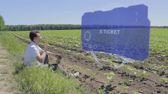 Man is working on HUD holographic display with text E-ticket on the edge of the field. Businessman analyzes the situation on his plantation. Scientist examines future technology