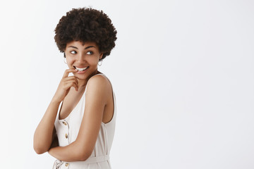 Studio shot of silly good-looking flirty African American female with afro hairstyle turning right with pleasure and desire smiling, biting fingernail with curious and intrigued expression