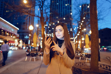 Beautiful girl in a evening city. Stylish brunette in a brown coat. Woman in a Chicago. Lady with a phone