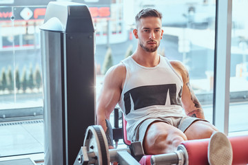 Strong focused man is doing legs exercises on training apparatus.
