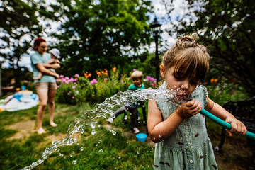 Girl drinking water from hose in yard