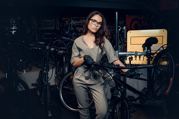 Fototapeta na wymiar Hardworking attractive woman is posing with bicycle at workshop.