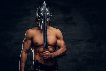 Strong gladiator with sword in his hands. He is wearing gladiator's bandage and helmet. - obrazy, fototapety, plakaty