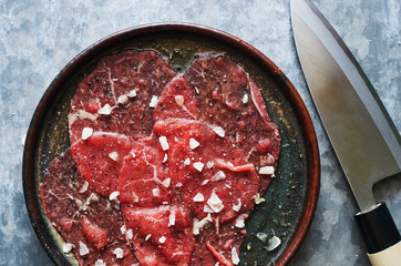 Raw homemade beef carpaccio with parmesan cheese in a plate with a Japanese knife top view close-up