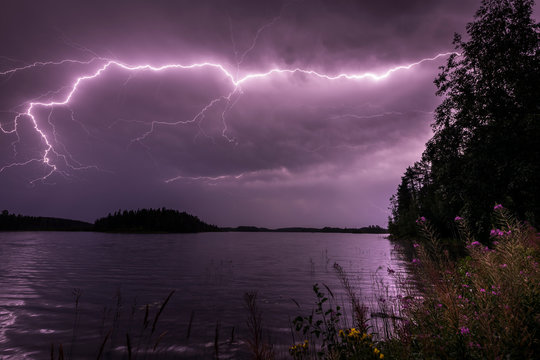 Purple lightning streak through clouds over water
