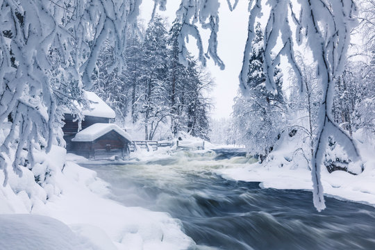 Old wooden house on river framed by snowy branches