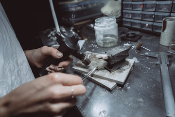 In the workshop, a woman jeweler is busy soldering jewelry