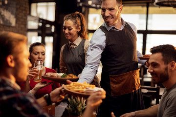 Young waiters serving lunch to group of friends in a pub.