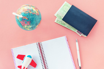 Notebook, toy airplane, pen, globe, passport and money on a pink background. Prepare for travel concept. Top view, flat lay. Soft focus.