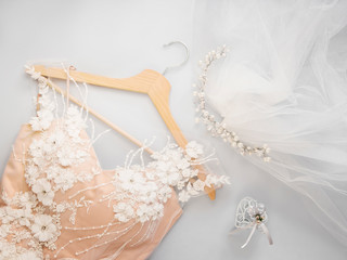 Minimal flat lay with wedding dress on hanger and veil with beads on light background. Sale wedding concept. Invitation template for celebration. Bride trendy cream color dress with flower.