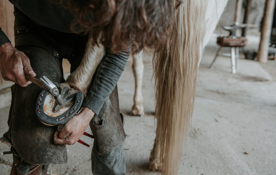 Unrecognizable adult man using knife to remove dirt from hoof of horse on ranch