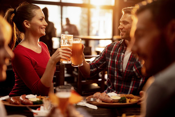 Happy couple toasting with beer while having lunch with friends in a restaurant.