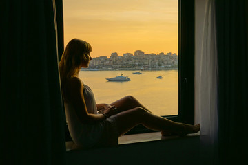 CLOSE UP: Woman relaxing on a window sill, looking through the window in Albania