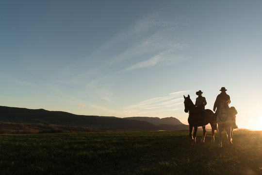 Man and woman riding horses against sunset sky on ranch