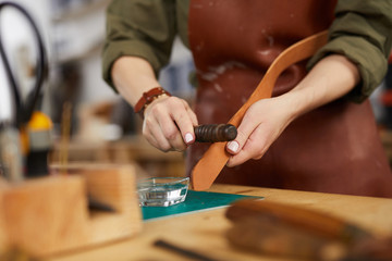 Closeup of unrecognizable craftsman working with leather in tannery shop, copy space