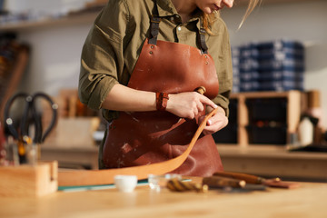 Mid section portrait of female craftsman working with leather in tannery shop, copy space