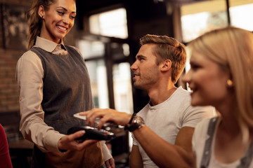 Young man making contactless payment via smart phone in a cafe.