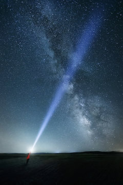 Night sky with majestic Milky way and person with bright upward beam of light