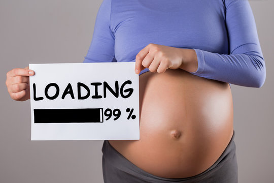 Image of close up stomach of pregnant woman holding paper with text loading on gray background.