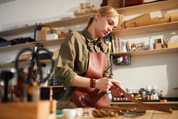 Waist up portrait of female craftsman working with leather in tannery shop lit by sunlight, copy space