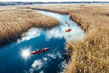 Group of people in kayaks among reeds on the autumn river. - obrazy, fototapety, plakaty